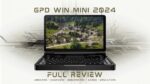 GPD WIN Mini 2024: Compacte handheld gaming PC gepresenteerd in open clamshell positie. 7-inch scherm met hoge resolutie met een levendige luchtfoto van een landelijk dorp met traditionele huizen en weelderig groen. Volledig QWERTY toetsenbord zichtbaar onder het scherm, wat wijst op dubbele functionaliteit voor gaming en productiviteit. Apparaat omringd door gestileerde printplaatpatronen die de technologische kracht benadrukken. Bovenaan staat &quot;GPD WIN MINI 2024&quot; en onderaan &quot;FULL REVIEW&quot;, met als subtekst &quot;UNBOXING - OVERVIEW - BENCHMARKS - GAMES - EMULATORS&quot;. De afbeelding combineert echte hardwarepresentatie met grafische elementen en suggereert een uitgebreide beoordeling van de mogelijkheden van het apparaat in verschillende gebruikssituaties. De zwarte behuizing contrasteert met de kleurrijke scherminhoud en benadrukt het slanke ontwerp en de draagbaarheid van het apparaat, terwijl het krachtige prestaties voor gaming en nog veel meer belooft.