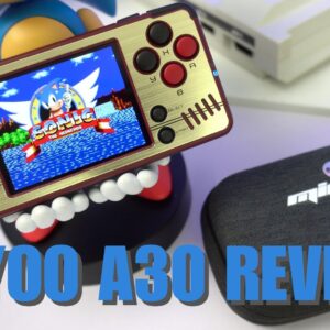 Ręczna konsola do gier w stylu retro, Miyoo A30, jest prezentowana w widocznym miejscu. Jej złoto-czarny design zawiera ekran przedstawiający Sonic the Hedgehog, otoczony klasycznymi kontrolerami do gier, w tym D-padem, okrągłymi przyciskami i drążkiem analogowym. Urządzenie jest podtrzymywane przez zabawną figurkę z widocznymi dużymi zębami. Na pierwszym planie znajduje się czarne etui ochronne z logo Miyoo A30. Obraz pokazuje kompaktowy rozmiar i nostalgiczny urok konsoli, podkreślając jej przenośność i klasyczne możliwości grania. Pogrubiony niebieski tekst na dole brzmi &quot;MIYOO A30 REVIEW&quot;, wskazując cel obrazu. Ogólna kompozycja podkreśla połączenie nowoczesnej technologii z estetyką gier retro, przemawiając do entuzjastów klasycznych gier wideo