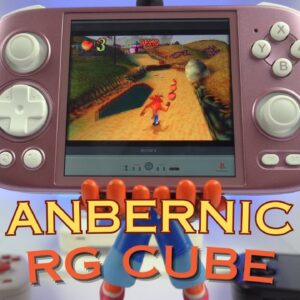 L&#039;immagine mostra una console di gioco portatile con la dicitura &quot;ANBERNIC RG CUBE&quot; in primo piano. La console ha un colore rosato ed è dotata di un D-pad, due stick analogici e diversi pulsanti, tra cui i tasti X, Y, A e B. Lo schermo della console mostra una scena di gioco tratta da &quot;Crash Bandicoot&quot;, in cui il personaggio corre lungo un percorso raccogliendo oggetti. La console sembra essere sorretta da una figura, forse un giocattolo o un modello, visibile sotto la console. Lo sfondo è caratterizzato da un ambiente moderno e pulito, illuminato di blu, e alcuni gadget tecnologici sono parzialmente visibili.