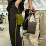 Two individuals wearing AYANEO leather crossbody bags, showcasing the green and brown color options. The bags are worn comfortably, demonstrating their practicality and portability.