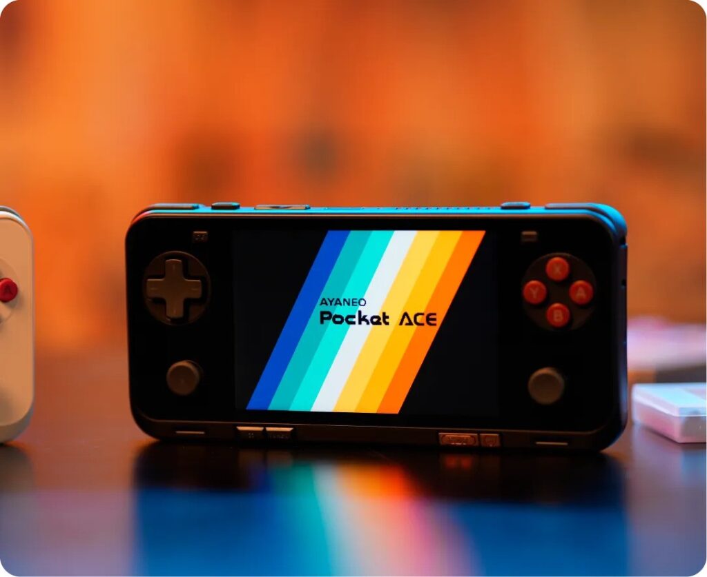 A handheld gaming console the AYANEO Pocket ACE displayed on a table with a colorful gradient logo on its screen The device features a D pad analog sticks and action buttons all illuminated in a warm ambient setting with a blurred orange background