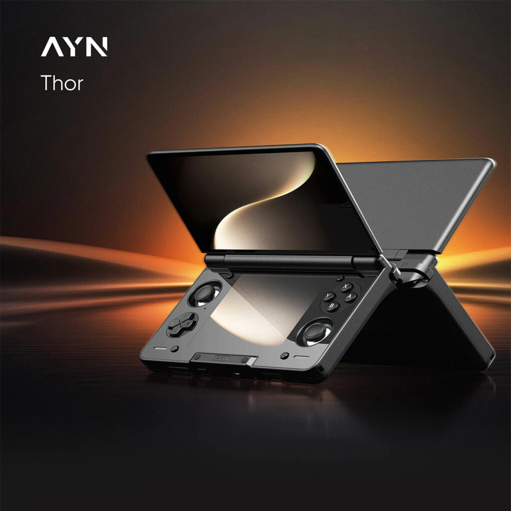 A sleek, black AYN Thor handheld gaming console is shown angled upwards, with its clamshell design open like a book, against a dark, glowing background. The screen is a glossy black, reflecting a soft golden light. The bottom half of the device is a matte black with a textured pattern and glossy finish on the controls, which include a D-pad, analog sticks, and face buttons. The AYN logo and "Thor" are in white text in the top left corner.
