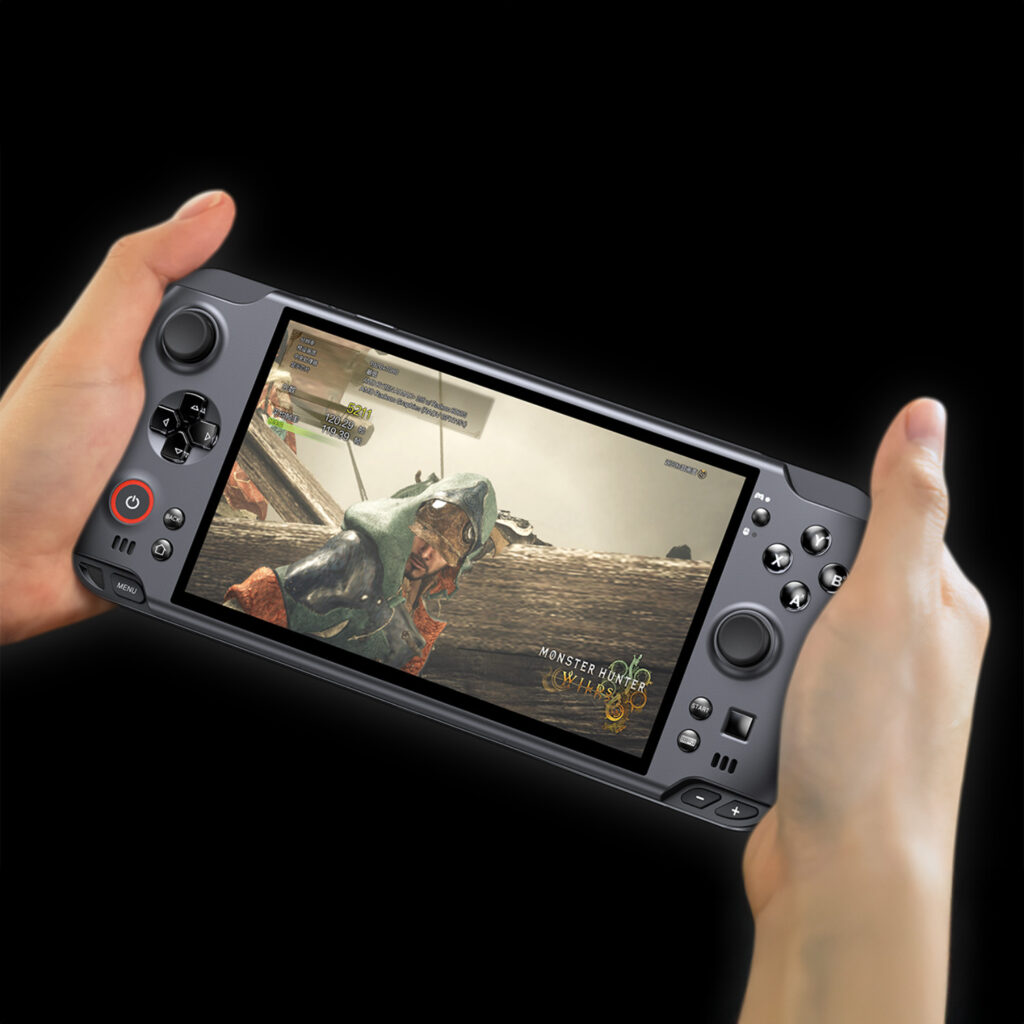 A pair of hands holding a dark grey GPD WIN 5 handheld gaming console isolated against a black background The console's widescreen display shows a scene from the video game "Monster Hunter: World", with a character and an enemy monster in a swampy environment. A transparent overlay on the screen shows performance stats like CPU, GPU, and FPS.